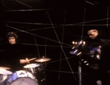 a man playing drums in a dark room with a few lights behind him