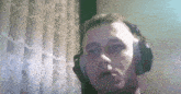 a man wearing headphones looks at the camera in front of a lace curtain