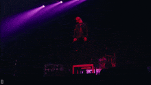 a man singing into a microphone on a stage with purple lights and the letter d below him