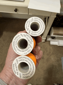 three spools of polyester embroidery thread are being held in someone 's hand