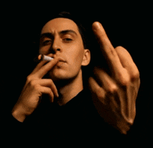 a man in a black shirt is smoking a cigarette and giving the middle finger .