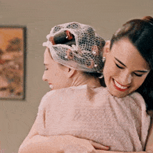 two women hugging each other with one wearing a hat
