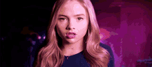 a young woman with long blonde hair and hoop earrings is making a funny face in front of a purple background .