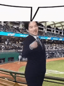 a man in a suit and tie is standing on a baseball field with a speech bubble above him .