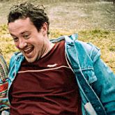 a man wearing a speedo shirt and a denim jacket laughs