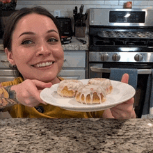 a woman holds a plate of cinnamon rolls in her hands