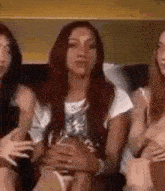 three women are sitting on a couch holding each other 's stomachs .
