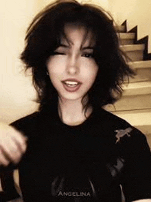a woman with short black hair is wearing a black shirt and making a face .