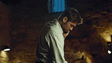 a man in a white shirt is talking on a cell phone in a dark room