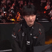 a man wearing a black jacket with a monster logo on the sleeve is standing in front of a crowd .