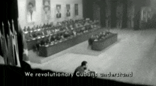 a man sits on the floor in front of a crowd with the words " we revolutionary cubans understand " below him