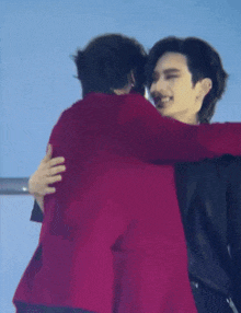a man in a red jacket is hugging another man in a black jacket .