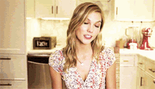 a woman in a kitchen wearing a floral shirt and a necklace