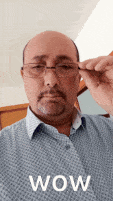 a man wearing glasses and a blue shirt with the word wow on the bottom