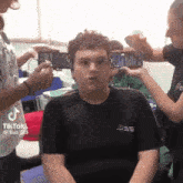 a man in a black shirt is being photographed by a group of people while sitting in a chair .