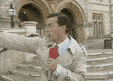 a man in a trench coat is holding a red microphone in front of a building