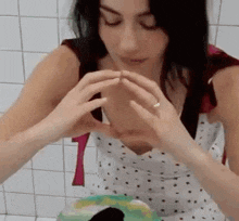 a woman is making a heart shape with her hands while sitting in front of a plate of food .