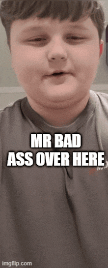 a young boy is wearing a gray shirt that says " mr bad ass over here "