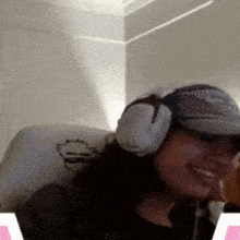 a woman wearing headphones and a hat is smiling in a room