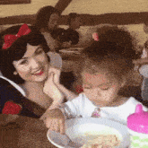 a little girl sitting at a table with a woman dressed as snow white