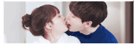 a man and a woman are kissing in front of a white wall .