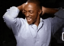 a man in a blue shirt is holding his hands behind his head and laughing .