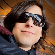 a man wearing sunglasses and a jacket with the letters ac on the bottom left