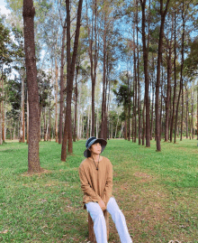 a woman in a hat sits on a tree stump in the middle of a forest