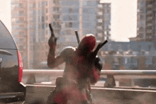 a man in a deadpool costume is holding two guns in front of a car in a city .
