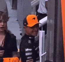 a man wearing an orange mclaren hat stands in front of a woman