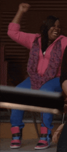 a girl in a pink jacket and blue pants is sitting on a chair and laughing