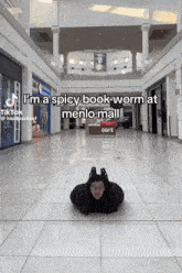 a man is crawling on the floor in a mall with the caption " i 'm a spicy book worm at meno mall "