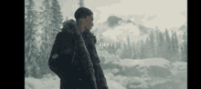 a man in a fur coat stands in a snowy forest with the letters zetz visible