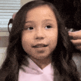 a little girl is getting her hair straightened by a woman in a pink hoodie