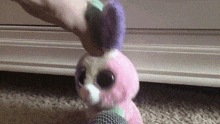 a pink and purple stuffed animal is being held by a person 's hand