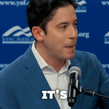 a man in a suit stands in front of a microphone and says it 's in white