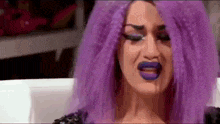 a woman with purple hair and purple lipstick is crying .