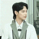 a man with a mullet is wearing a white coat and tie .