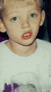 a young boy with blue eyes and red lipstick is wearing a white shirt