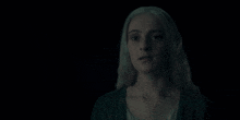 a woman with blonde hair is standing in the dark and looking at the camera