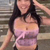 a woman in a purple crop top is standing in front of a crosswalk and smiling .