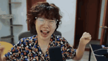 a woman wearing glasses and a floral shirt laughs with her fist in the air