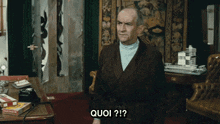 a man in a suit is sitting in a room with quoi written on the screen