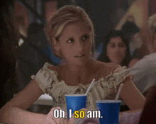a woman sitting at a table with two cups of soda and the words oh i so am