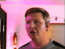 a man is making a surprised face in front of a pink wall