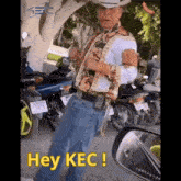 a man wearing a cowboy hat is standing in front of motorcycles and says hey kec