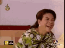 a woman in a green and white floral shirt is laughing on a tv screen
