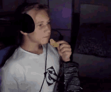 a young man wearing headphones is eating a snack while holding a bag of chips .