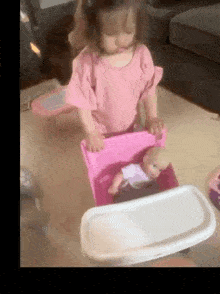 a little girl is playing with a doll in a pink box on the floor .