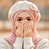 a woman wearing a pink hijab and a white hat covering her mouth with her hands